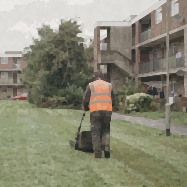 A grounds worker mowing the grass on a housing estate